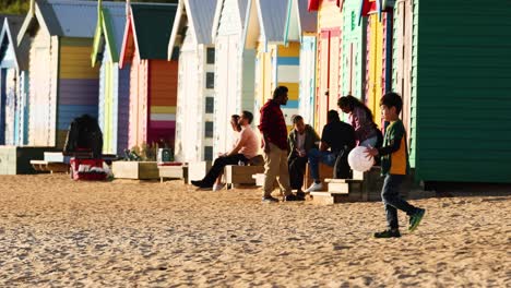 family playing with a ball near colorful beach huts