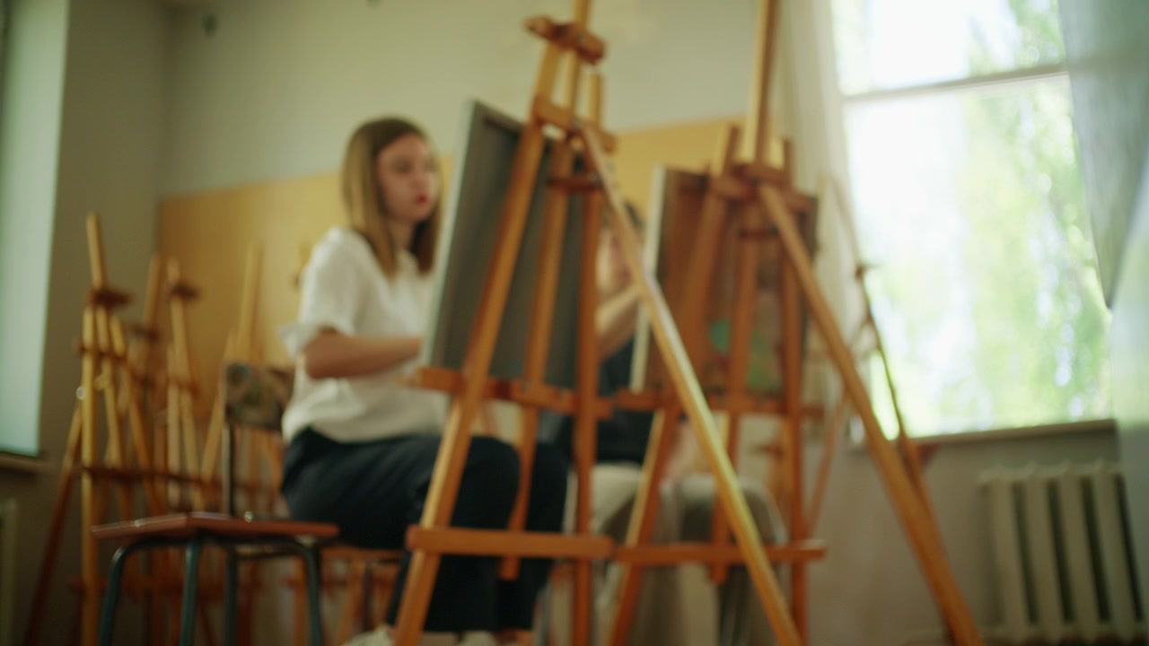Kunststuderende sidder ved staffelier og øver tegneteknikker under et kreativt værksted.