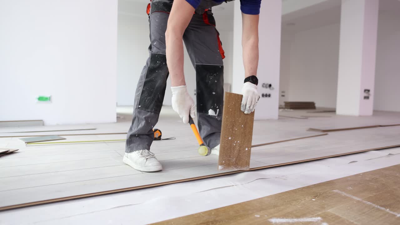 Construtor assenta réguas de piso laminado martelando a borda no chão