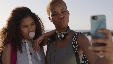 two girlfriends taking selfies blowing bubblegum having fun on sunny beach