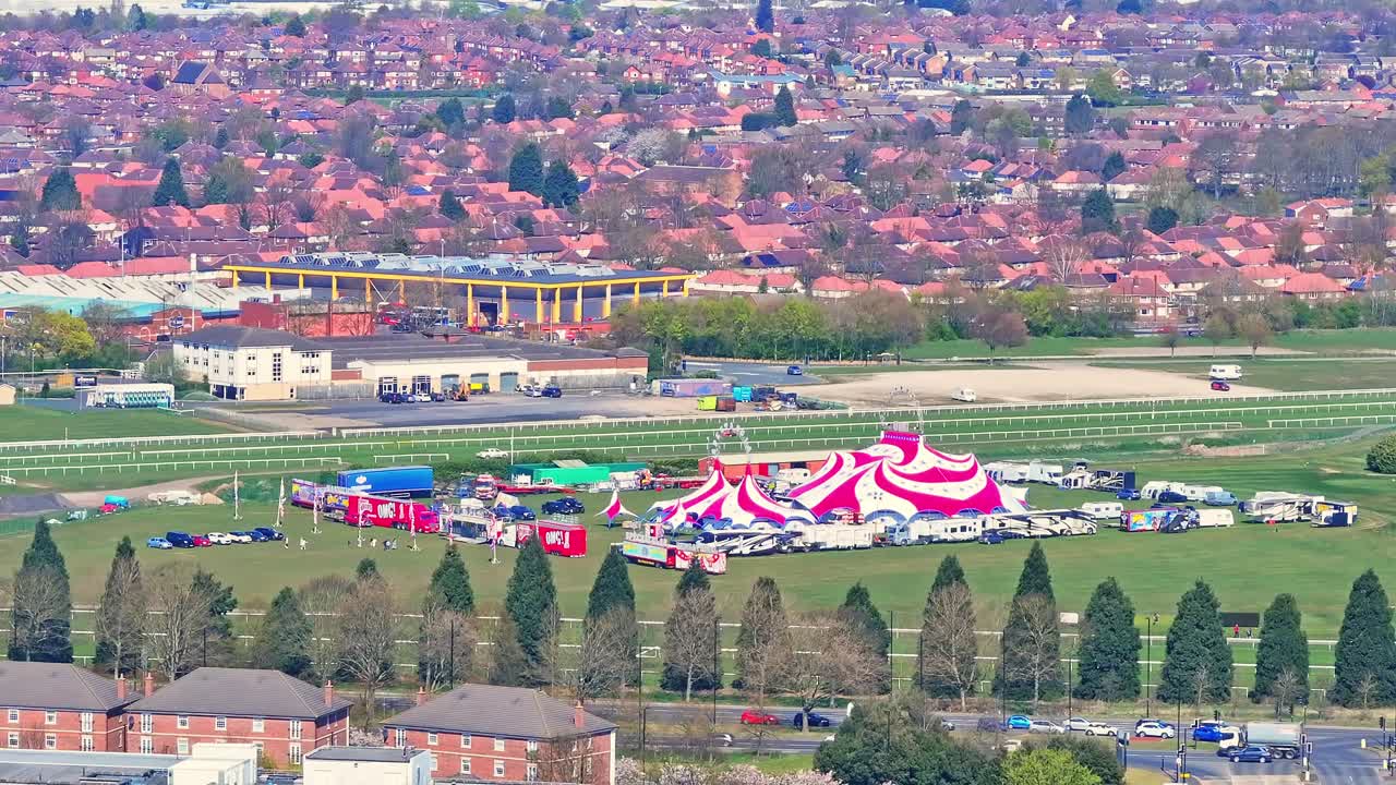 Doncaster Racecourse with a red and white circus tent, trailers, and setup on the grassy field, backed by the grandstand and dense residential area in Doncaster, South Yorkshire, England, aerial view