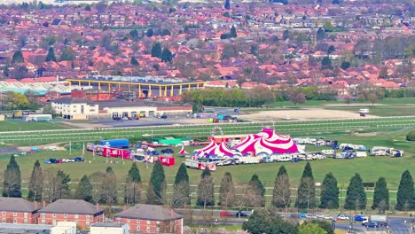 doncaster racecourse with a red and white circus tent, trailers, and setup on the grassy field, backed by the grandstand and dense residential area in doncaster, south yorkshire, england, aerial view