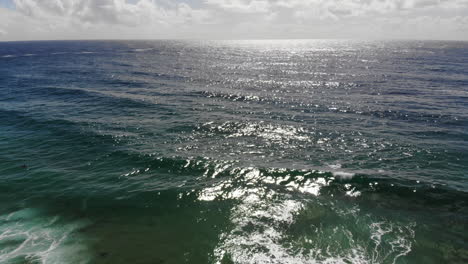 vista aérea de las olas del océano azul profundo, el reflejo del sol y las nubes en el fondo