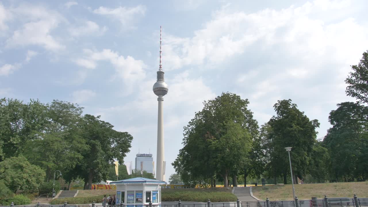 cámara lenta pasando por la torre de televisión en berlín en un día de verano con hojas verdes en los árboles