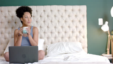 montaje de una mujer biracial usando una computadora portátil y un teléfono inteligente en casa, en cámara lenta