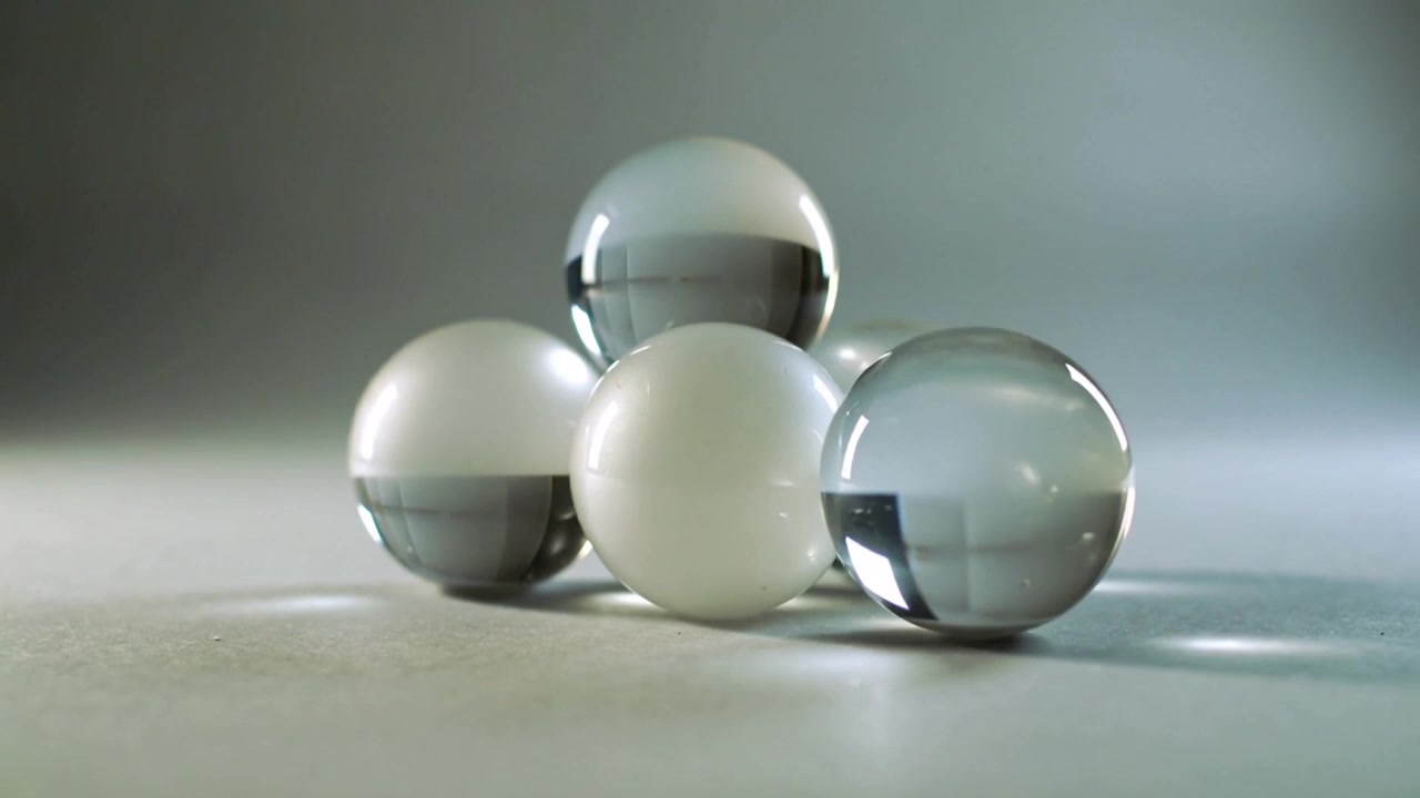 Pulling camera revealing two clear and two white spheres on textured tabletop, showing reflections