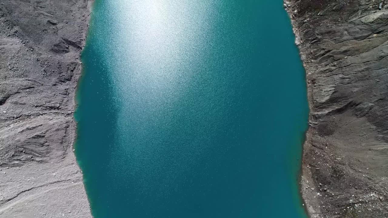 Stunning aerial shot of a turquoise glacial lake surrounded by rugged terrain. Ideal for travel blogs, prints, and nature documentaries
