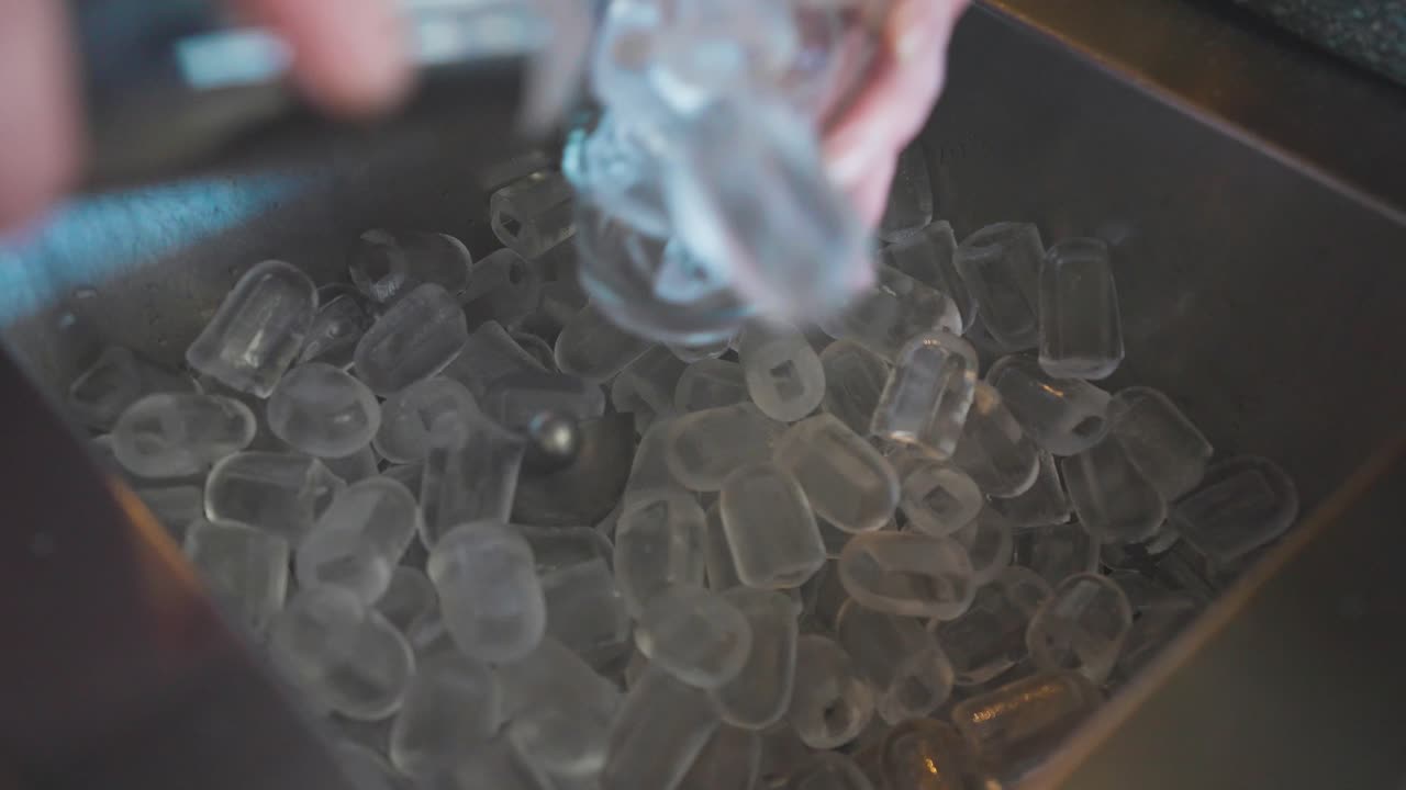Scooping up ice cubes with stainless steel shaker into glass, cocktail making