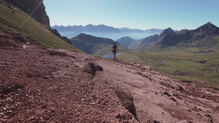 Back view of young hiker walking on red landscape towards a lake and enjoy the views of Pyrenees mountains