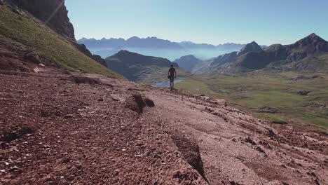 Rückansicht-Eines-Jungen-Wanderers,-Der-Auf-Einer-Roten-Landschaft-Zu-Einem-See-Geht-Und-Die-Aussicht-Auf-Die-Berge-Der-Pyrenäen-Genießt