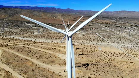 Windmills,-wind-turbines,-aerial-4k-drone-slow-pull-back-from-shot-down-line-of-spinning-blades,-energy,-green,-renewable,-power-generating-farm-on-desert-hills,-Palm-Springs,-Coachella,-Cabazon,-CA