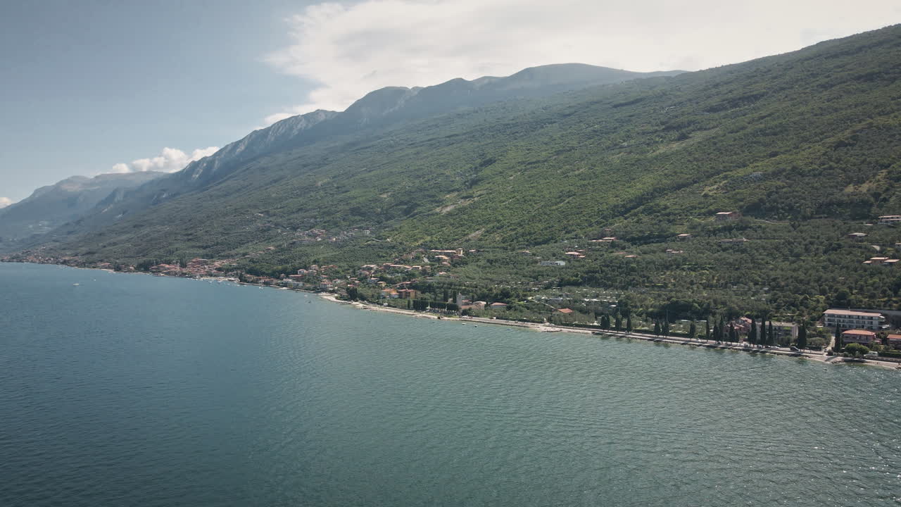 Volo dinamico con drone 4K UHD che avanza inseguendo un motoscafo bianco sulle acque turchesi del Lago di Garda, Italia. Perfetto per viaggi di lusso, stile di vita nautico e pubblicità estive