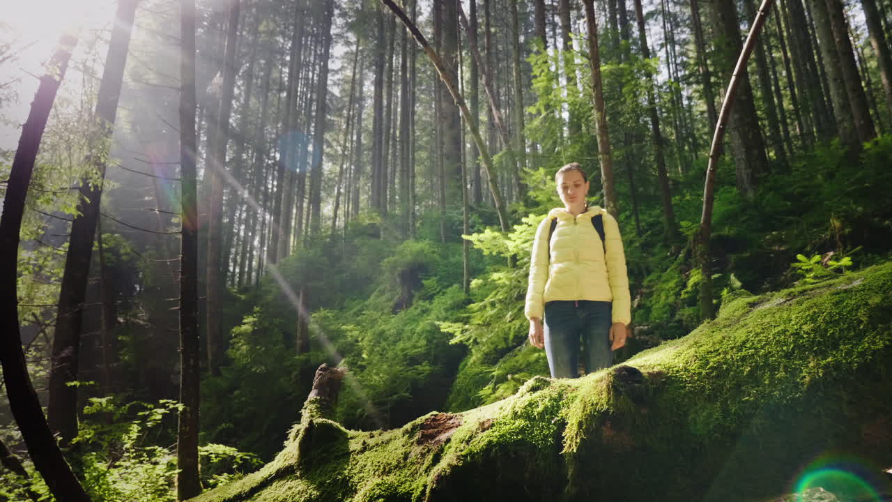 다운 재킷을 입고 배낭 끈을 묶은 여성 여행자가 신발에 끈을 묶고 나무에 서 있다