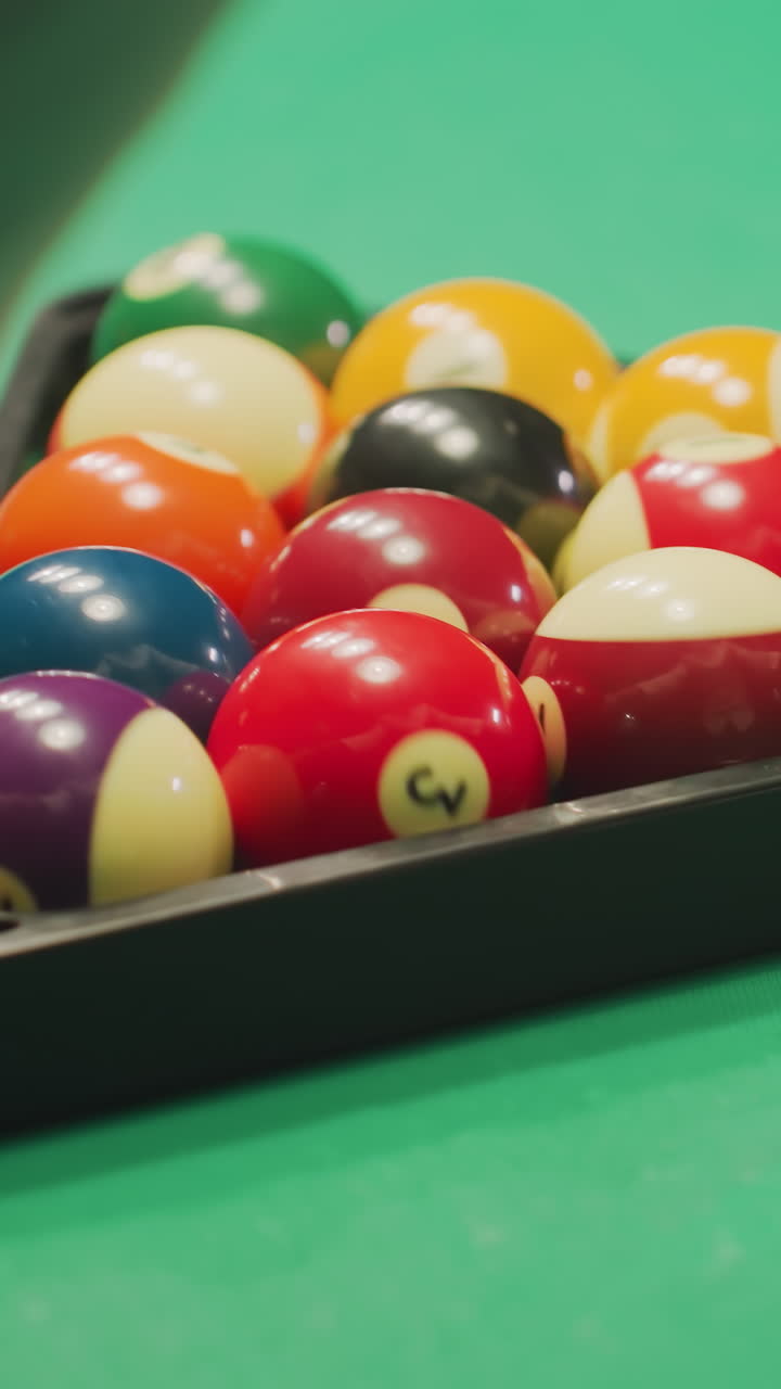 Primo piano da dietro di una mano di un giovane che indossa una camicia bianca e che muove delicatamente una serie ben disposta di colorate palle da biliardo in formazione triangolare su un tavolo da biliardo verde