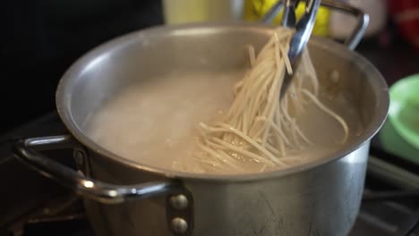 chef tossing pasta noodles in a pot of boiling water using tongs