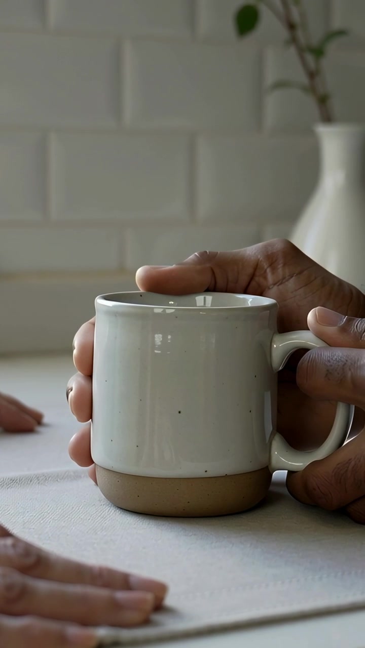 Vertical video: Bringing right-hand person steadying ceramic mug at kitchen counter, offering drink