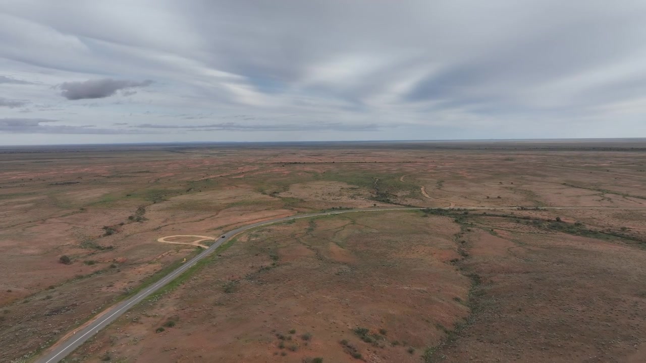 Tomada de rastreamento aérea de drone seguindo um veículo ao longo de uma estrada remota sinuosa através da vasta paisagem do outback perto de Silverton e Broken Hill, Nova Gales do Sul, Austrália