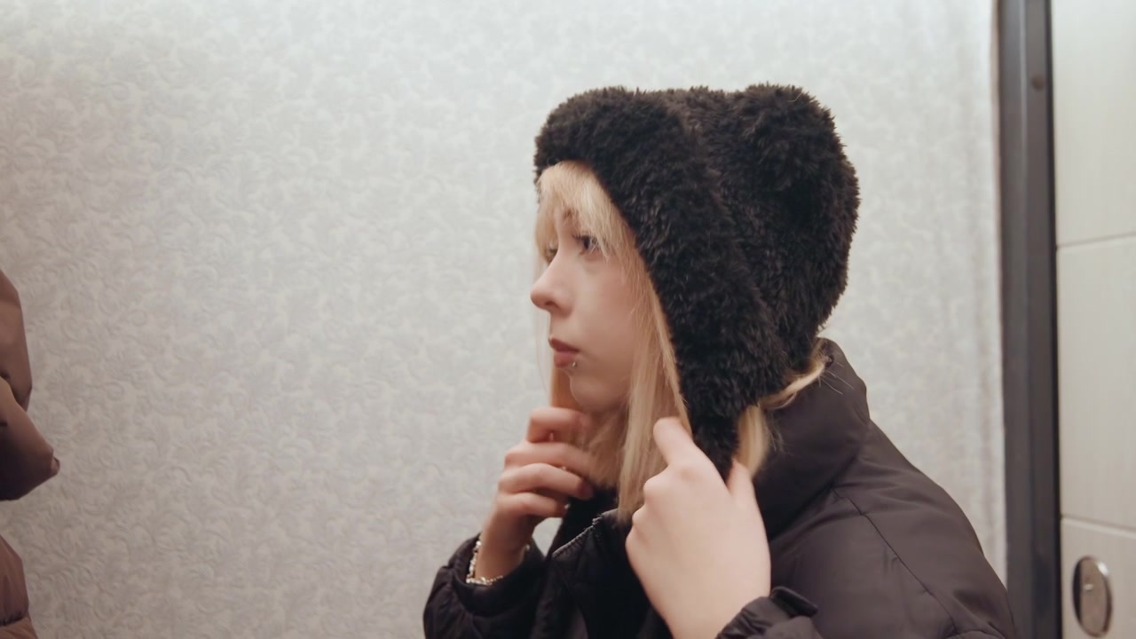 Blonde woman ready for cold winter journey. Securement of hood strings prior to outdoor winter travel. White woman ensuring her furlined hood is properly adjusted for winter commute
