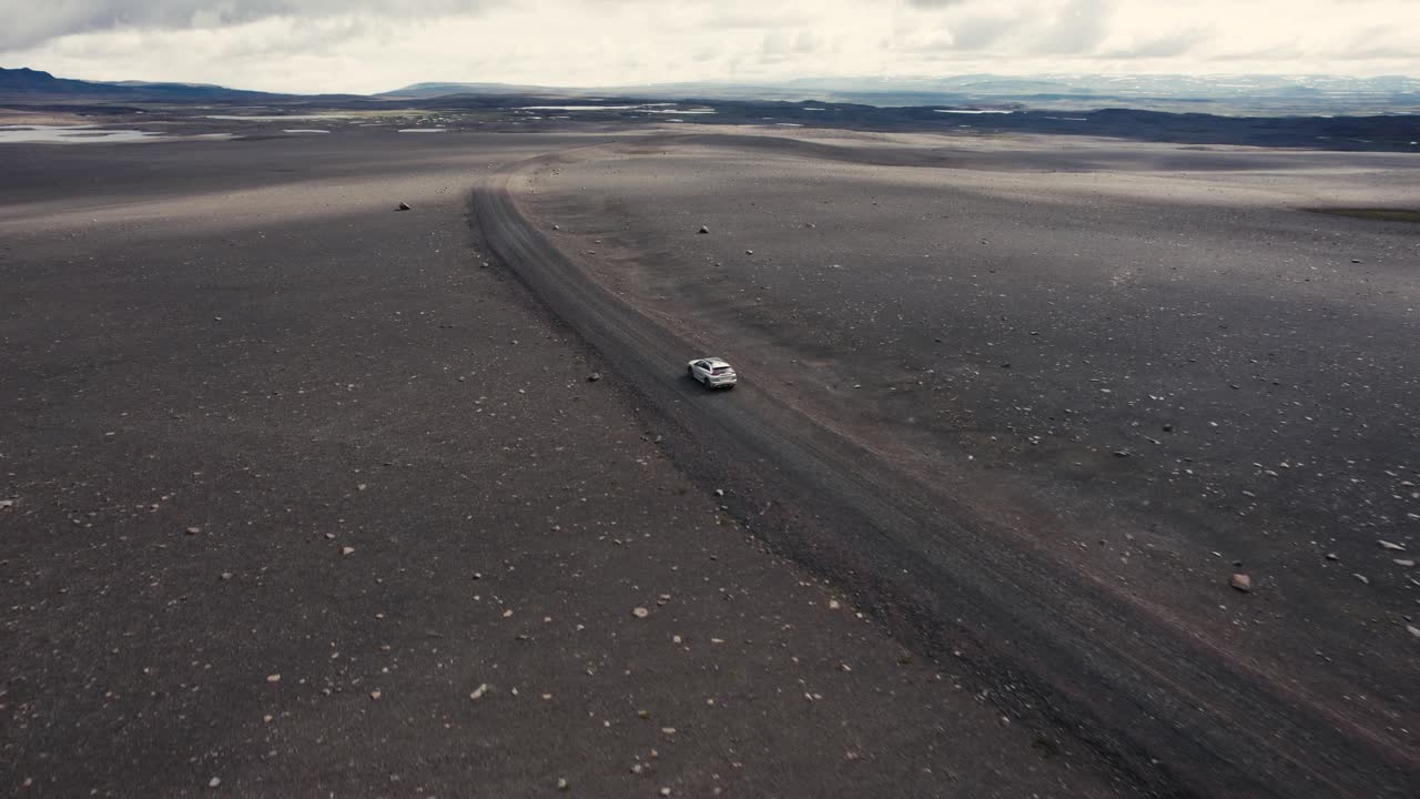 dron siguiendo un coche plateado con la cámara inclinándose lentamente conduciendo fuera de la carretera en el campo lunar de islandia 4k
