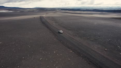 Drohne,-Die-Einem-Silbernen-Auto-Folgt,-Wobei-Die-Kamera-Langsam-Nach-Oben-Kippt-Und-Im-Mondähnlichen-Hinterland-Von-Island-4k-Fährt