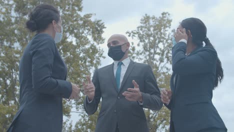 business colleagues in face masks meeting outside, greeting each other with elbows bumps and talking