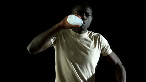 Handsome-man-jogging-and-drinking-water-against-black-background