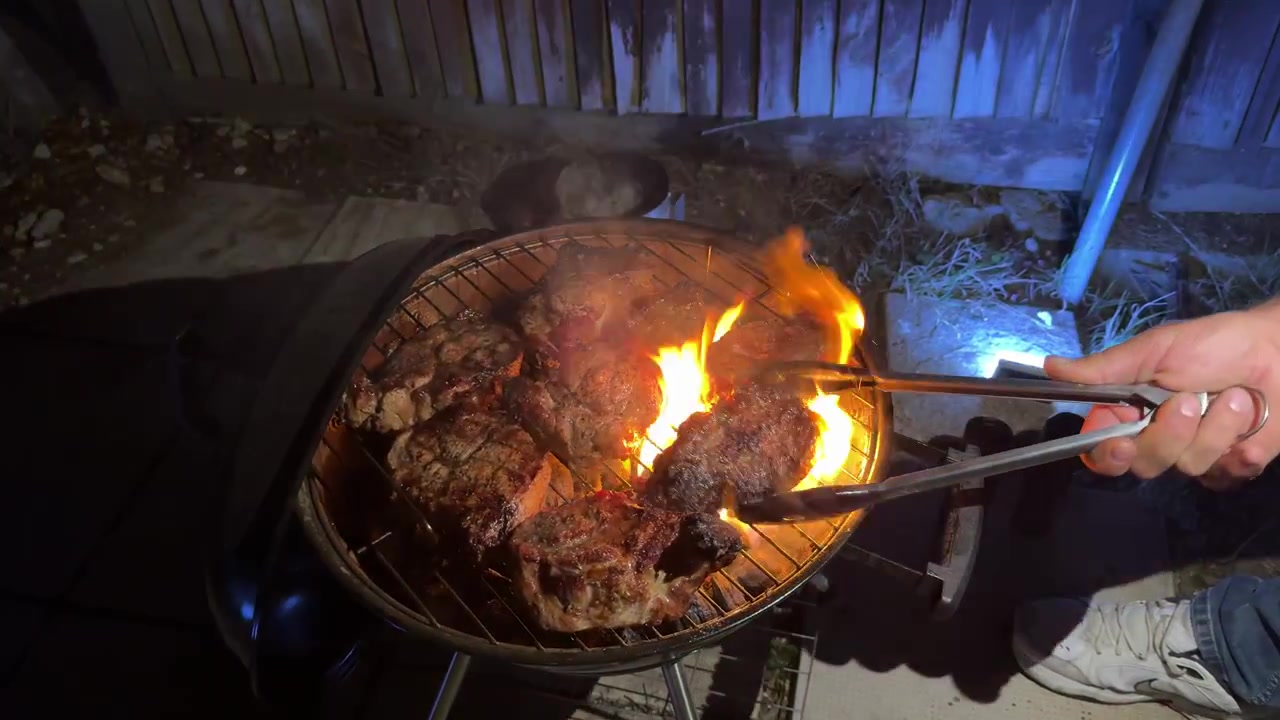 Bifes grelhando em uma churrasqueira a carvão com chamas à noite em Gosport, Inglaterra