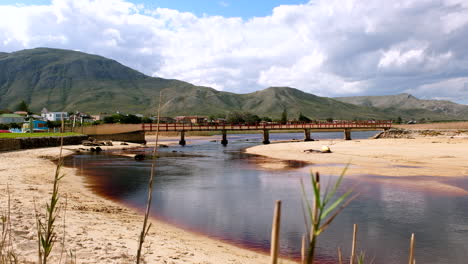 Riser-behind-coastal-reeds-reveals-flow-of-Kleinmond-lagoon-water-and-red-bridge