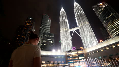 female tourist take smartphone picture of illuminated petronas towers at night
