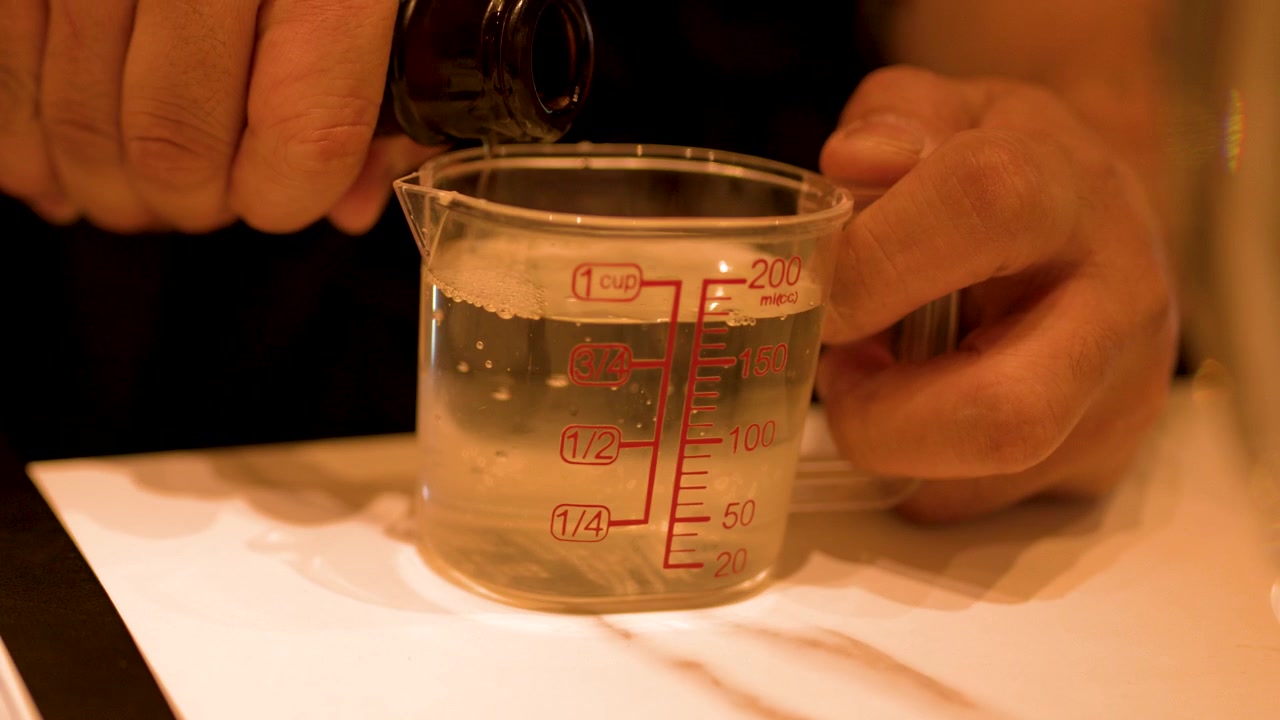 ボトルからプラスチック製の計量カップに日本酒を注いでいる手のクローズアップ。