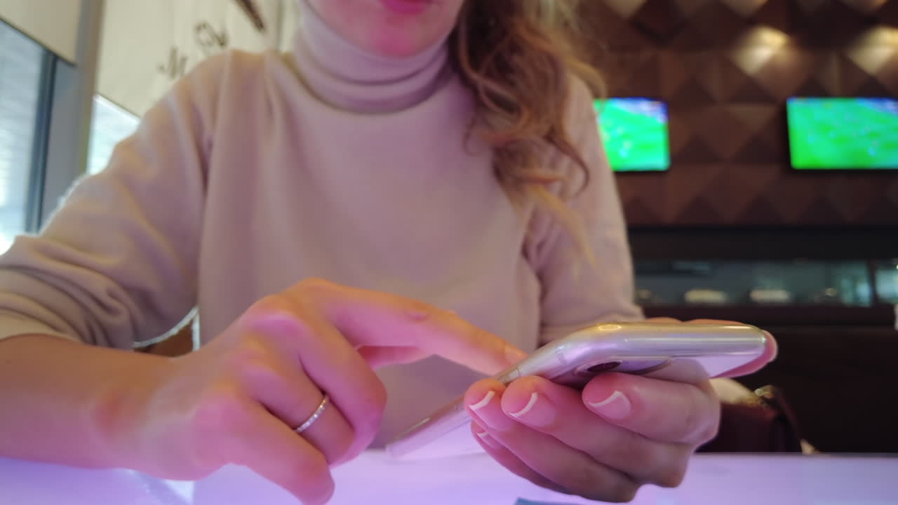 Woman working on mobile phone at a restaurant, tv screens with soccer