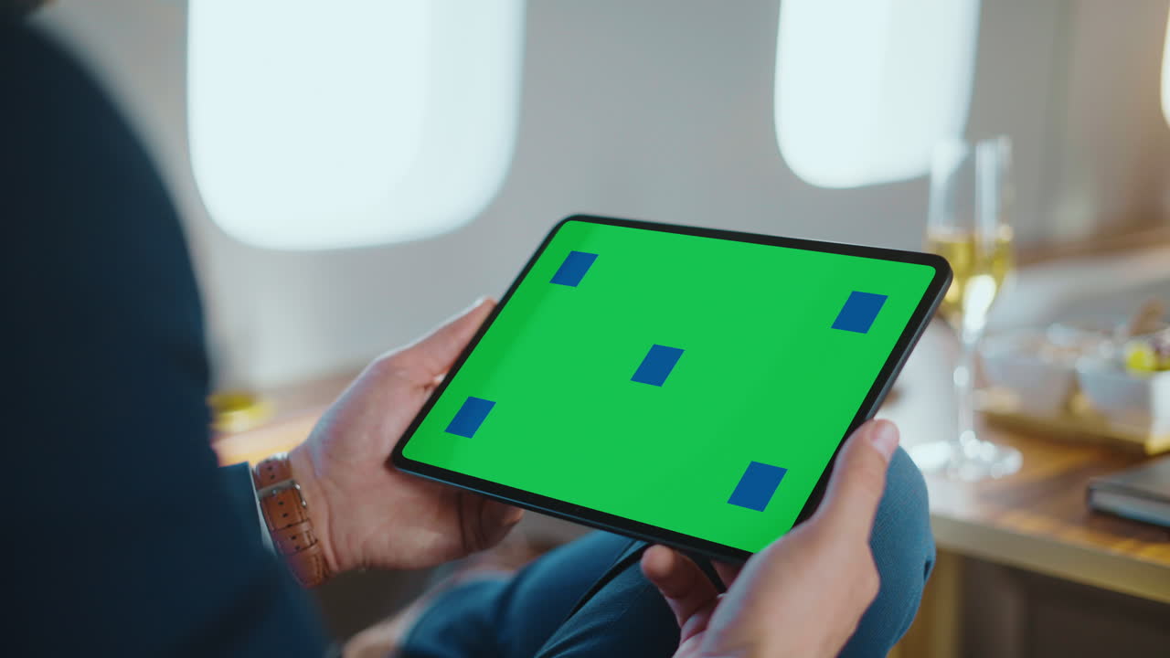Person holding a tablet with a green screen on an airplane