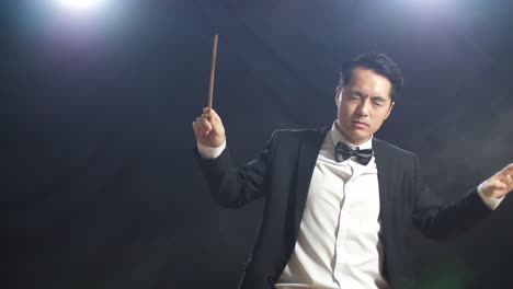 conductor asiático hombre sosteniendo un bastón cerrando los ojos y mostrando el gesto rápidamente en el estudio negro con niebla