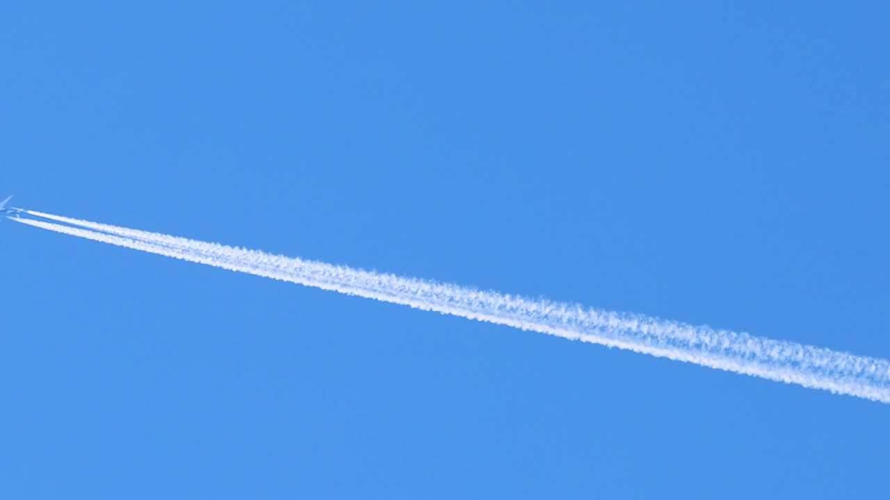 A jet plane leaves a distinct white contrail across a bright blue sky, showcasing high-altitude flight.