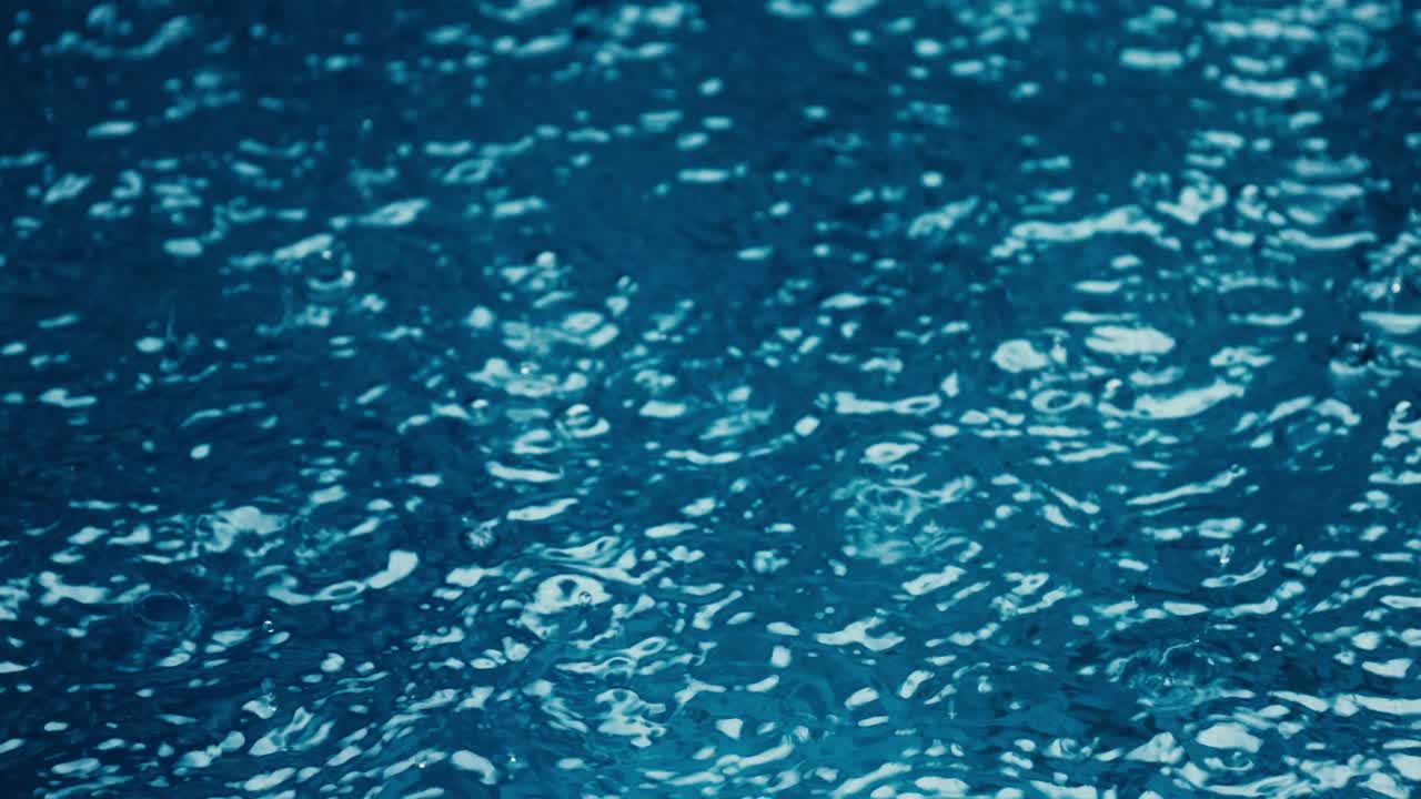 Close-up Pouring down rain during monsoon in blue water swimming pool in Bali, Indonesia