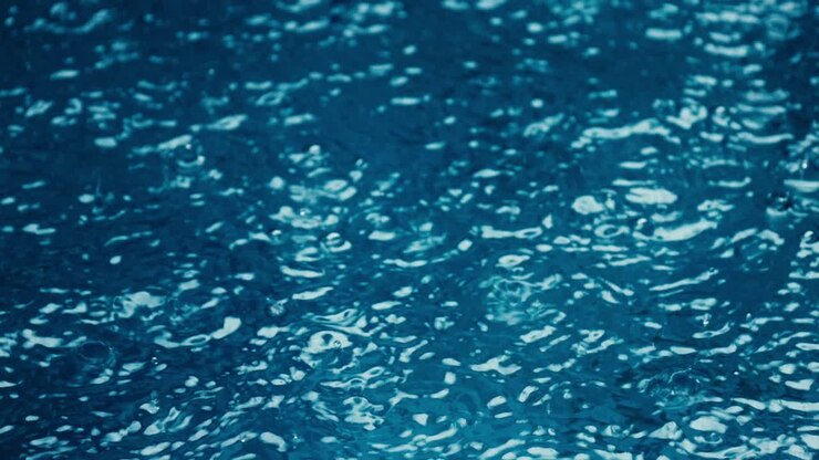 Primo piano della pioggia scrosciante durante il monsone in una piscina dall'acqua blu a Bali, Indonesia.