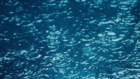 close-up pouring down rain during monsoon in blue water swimming pool in bali, indonesia