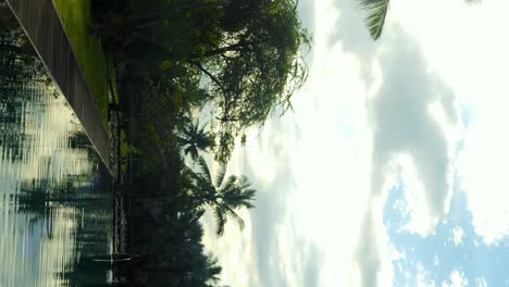 Establecimiento-En-Cámara-Lenta-Vertical-Toma-De-Una-Hermosa-Piscina-Al-Amanecer-En-Bali-Indonesia-Con-Vistas-Al-Jardín-Verde-Con-árboles-Y-Palmeras-Durante-Un-Gran-Viaje