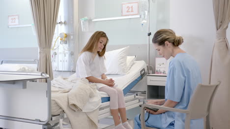 caucasian female doctor talking with girl patient sitting on hospital bed, slow motion