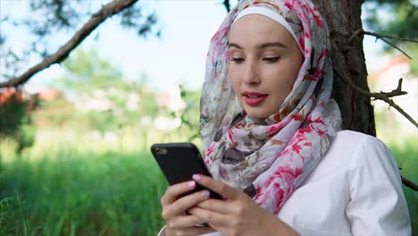 woman in hijab using smartphone in a park