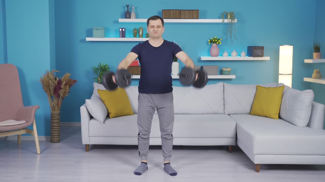 강한 남자는 집에서 덤벨의 도움으로 몸을 구축합니다.