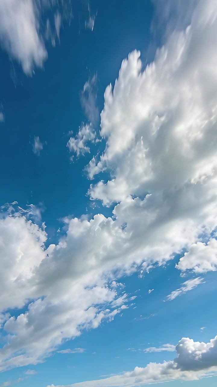 Video verticale: Telecamera inclinata e brezza che muove una grande massa di cumuli attraverso il cielo blu con una scia di condensazione.