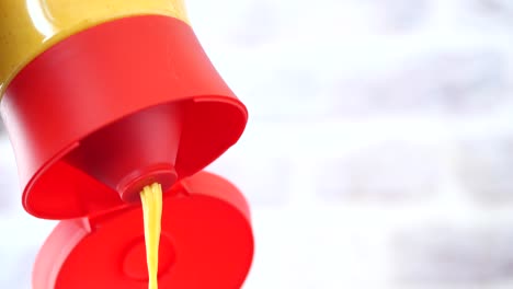 primer plano de una botella de mostaza vertiendo mostaza amarilla sobre un fondo blanco