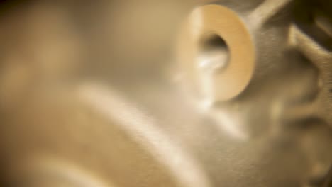 held within the frame of a handheld camera, a close-up reveals a circular threaded hole centered in a shiny metallic object with a textured surface, standing against a blurred, out-of-focus background