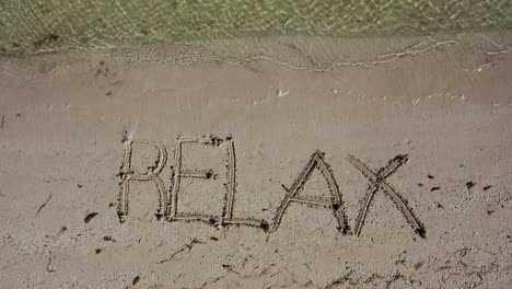 relax written in the sand at an angle and gets smaller as aerial camera rises