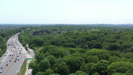 An-aerial-view-over-a-busy-parkway-next-to-a-large-park-with-green-trees