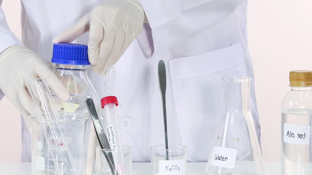 A scientist in gloves arranges various labeled bottles and test tubes on a laboratory table.