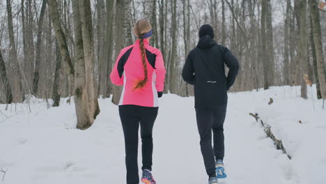 positive beautiful young healthy couple running with sportswear through the forest in the sunny winter morning. the view from the back