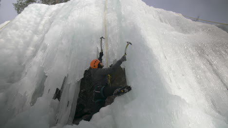 an adventurous man ice climbing up a sheer frozen rock face