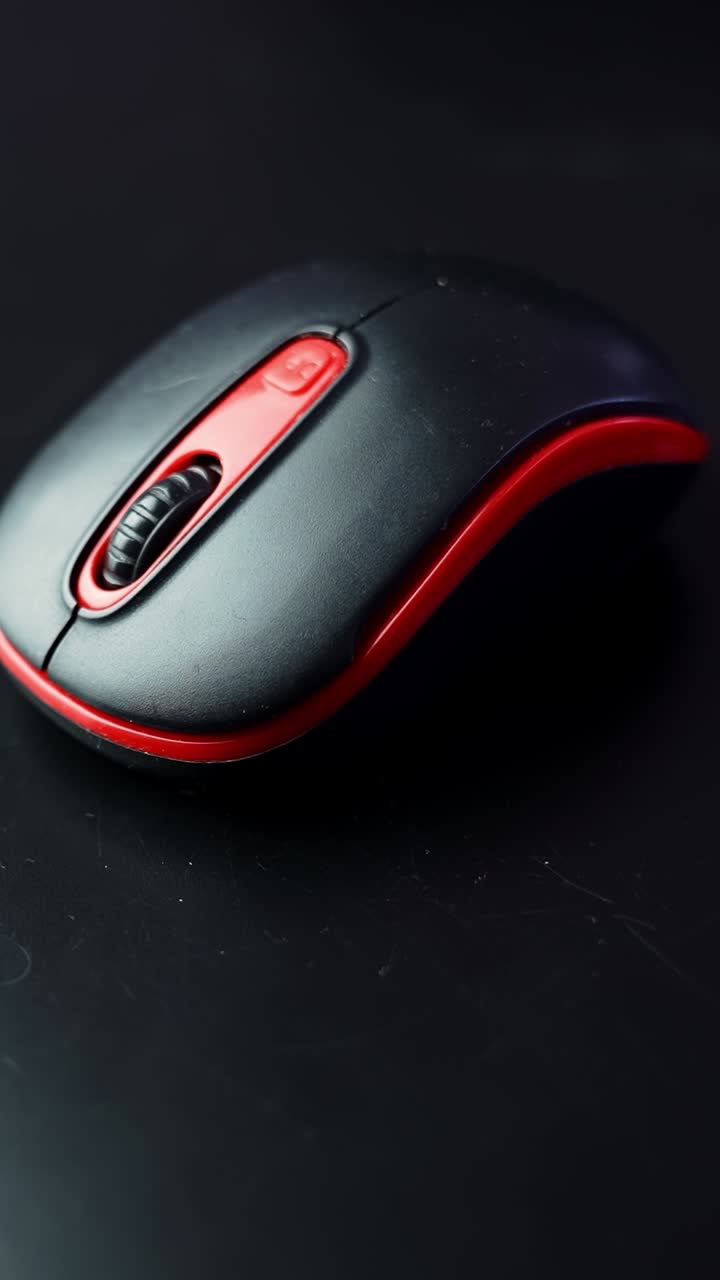 Moody macro shot of a black and red computer mouse on a dark desk with copy space, showing the scroll wheel and buttons in warm studio light. Vertical